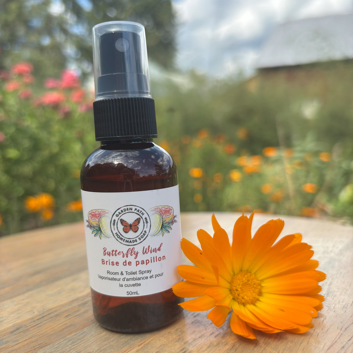 50 mL Butterfly Wind Room & Toilet Spray bottle by Garden Path Homemade Soap on a wooder surface with calendula flower. 100% Natural Essential Oil Blend