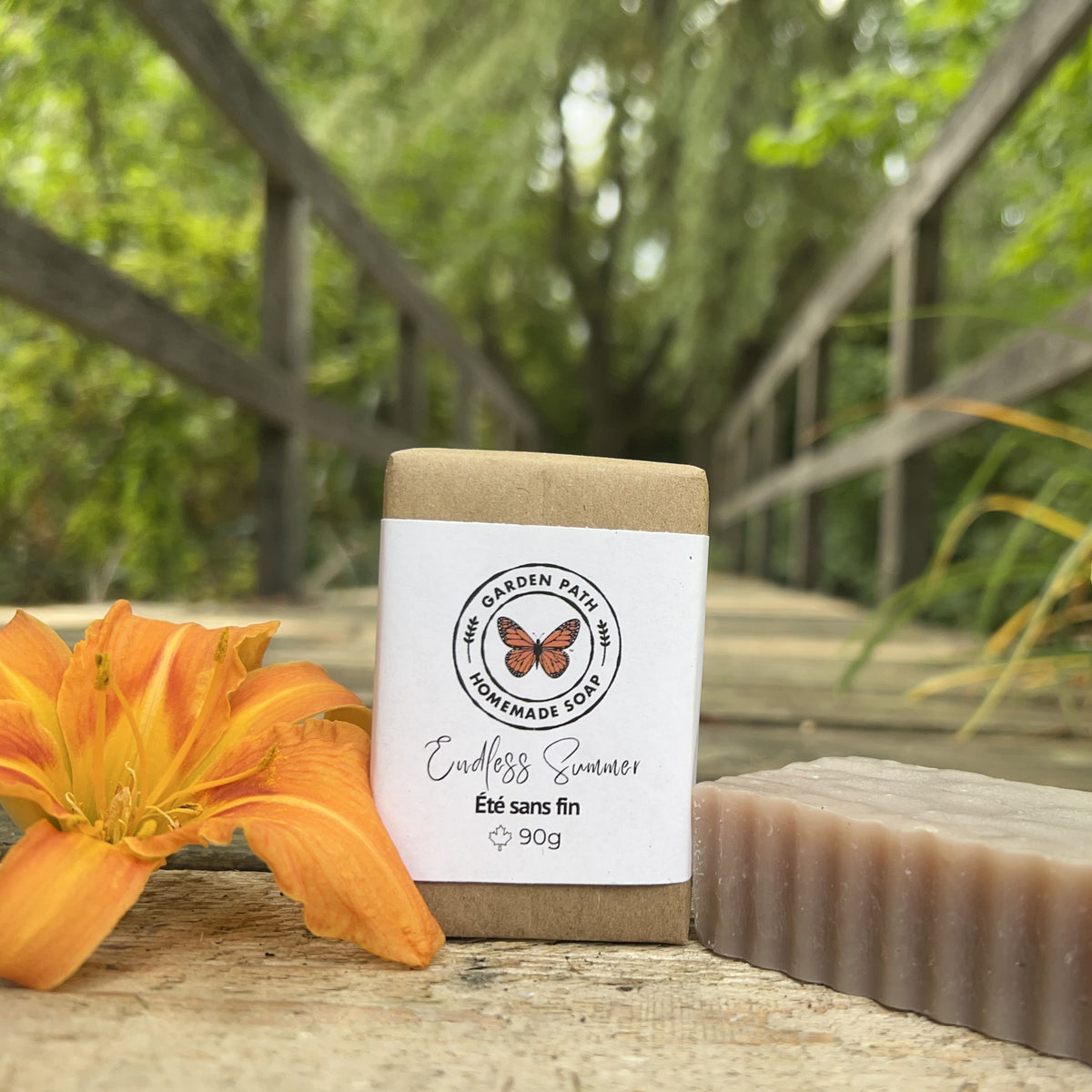 Endless Summer Bar of soap with a label featuring a butterfly and text, placed on a wooden surface with an orange flower and blurred green background.