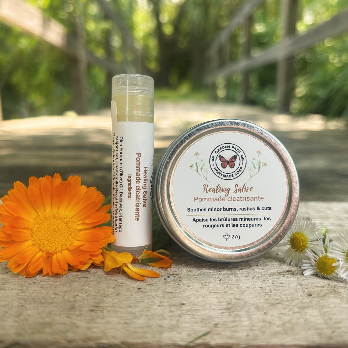 Healing Salve tube and tin on a wooden surface with flowers by Garden Path Homemade Soap. 100% Natural Ingredients & Essential Oils
