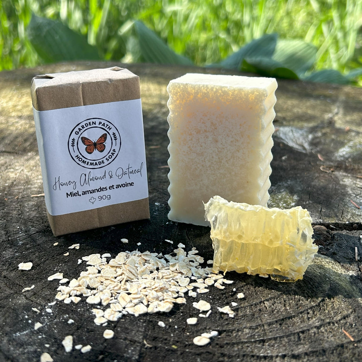 Honey Almond & Oatmeal Bar Soap on a wooden surface with oatmeal flakes and honeycomb beside the wrapped bar of soap | Gentle Exfoliating Bar Soap - Garden Path Homemade Soap