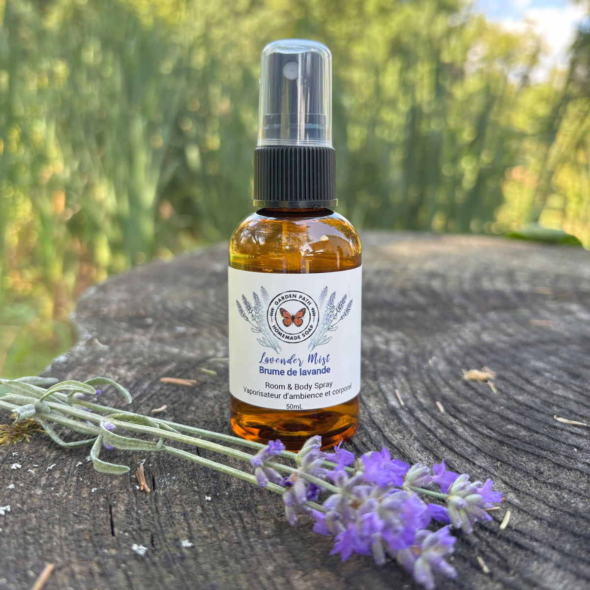 Garden Path Homemade Soap's Lavender Mist body sprayer sitting on a wooden surface with a sprig of lavender - 100% Natural Essential Oil