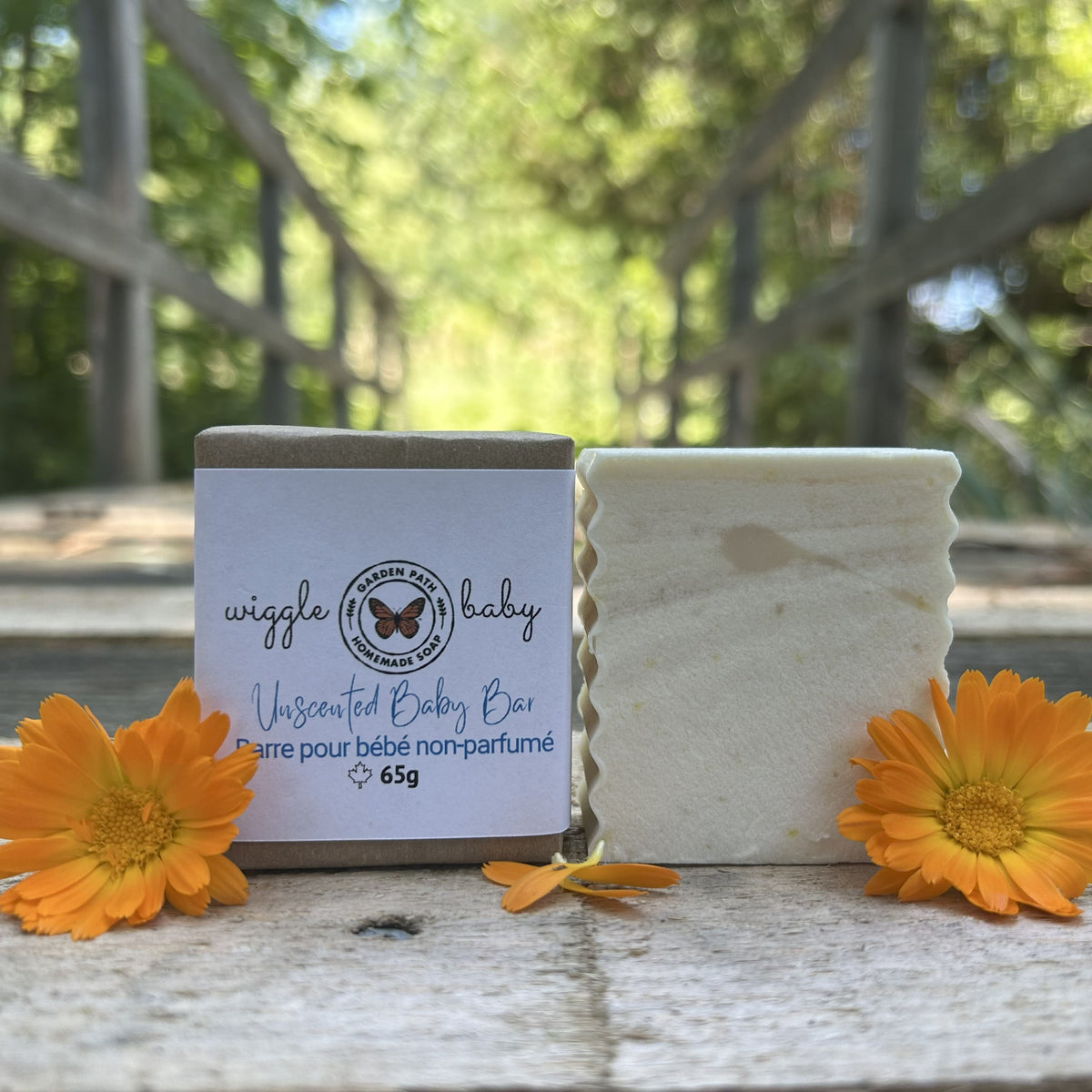 Wiggle Baby Bar both wrapped and unwrapped by Garden Path Homemade Soap sitting on a wooden surface with calendula flowers. 100% Natural Ingredients | Unscented