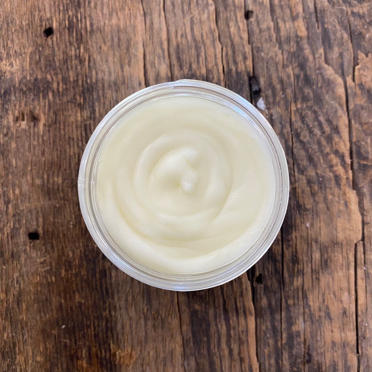 Opened jar of Garden Path Homemade Soap's Honey Almond Lotion on a wooden board by Garden Path Homemade Soap