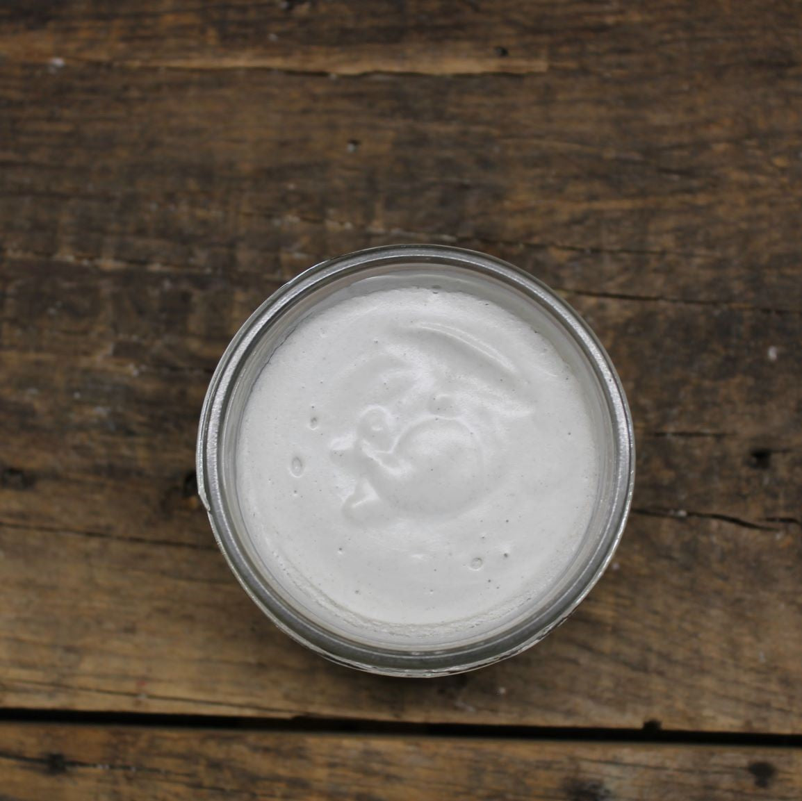 Open jar of shaving cream on a wooden surface by Garden Path Homemade Soap.