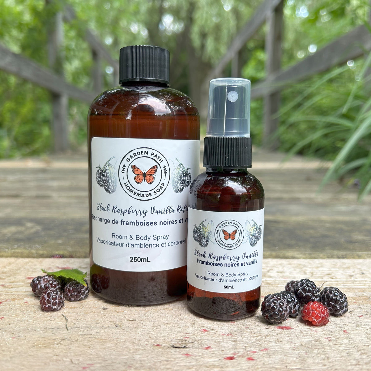 Black Raspberry Vanilla  Body & Room Sprayer and refill bottle by Garden Path Homemade Soap on a wooden surface with black raspberries.