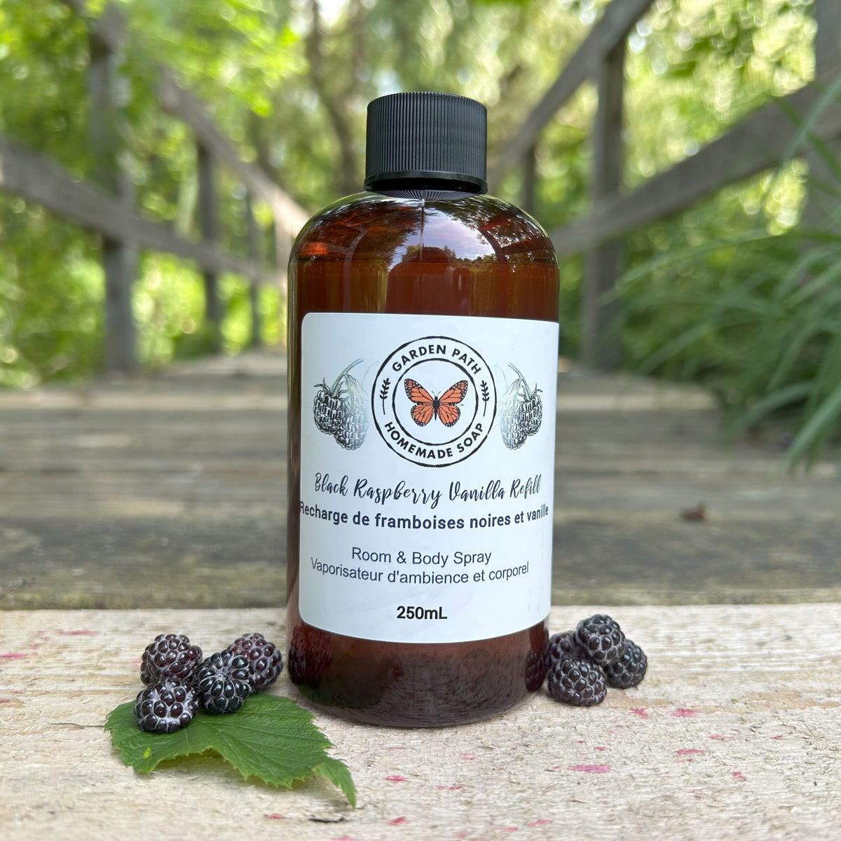 Black Raspberry Vanilla Room and Body spray refill  bottle 250ML by  Garden Path Homemade Soap on a wooden path with black raspberries.