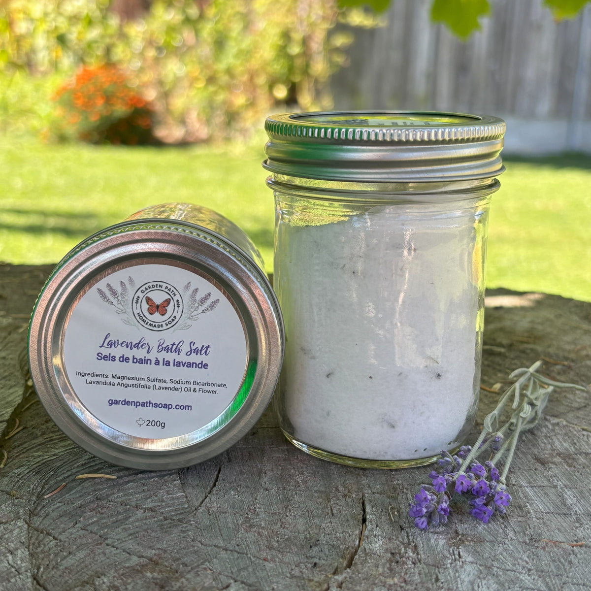 Jar of lavender bath salt with a label on a wooden surface outdoors by Garden Path Homemade Soap. 100% Natural Essential Oil & Ingredients