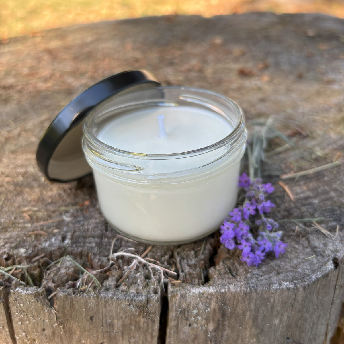 Small Lavender Candle opened sitting on a wooden surface with lavender beside it
