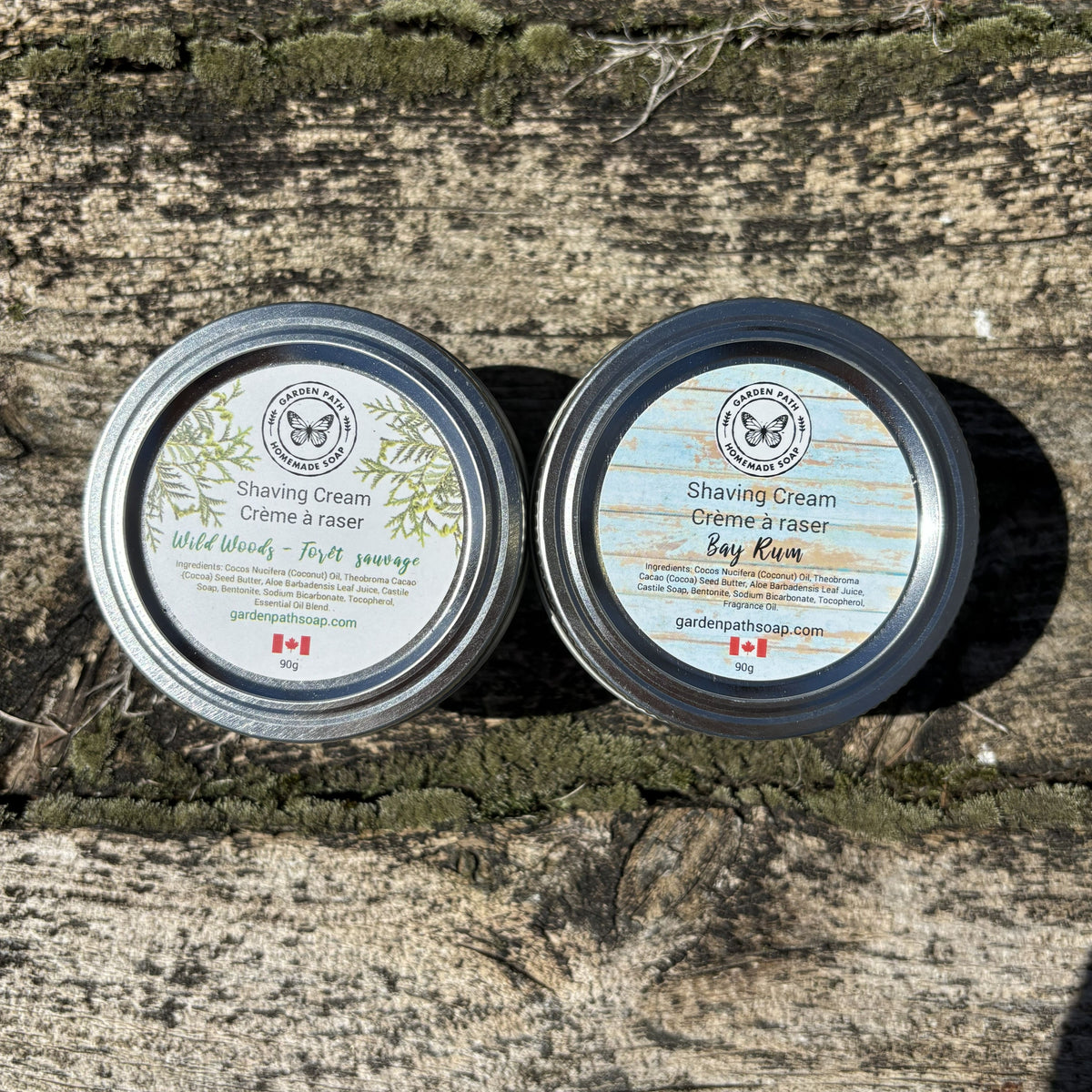 Two tins of shaving cream (Wild woods and Bay Rum) on a wooden surface by Garden Path Homemade Soap