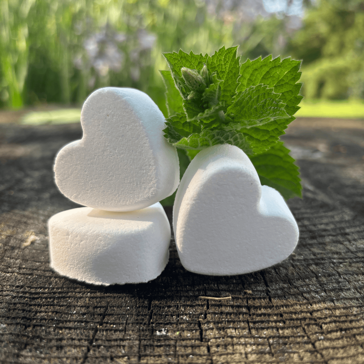 3 heart shaped Foot Fizzes on a wooden surface with peppermint springs by Garden Path Homemade Soap. 100% natural ingredients