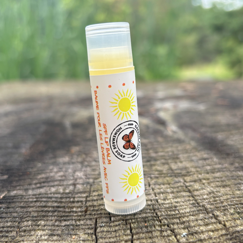 A stick of SPF lip balm  placed on a wooden surface with a natural background by Garden Path Homemade Soap. 100% Natural Ingredients