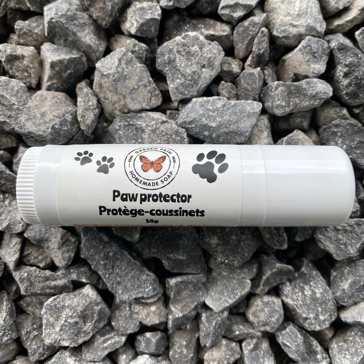A roll-up tube of paw protector cream placed on a bed of rocks, with the product's branding and text visible on the tube.